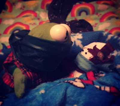 ID: a masked Kermit the Frog as John the Baptizer baptizes a masked snowperson as Jesus. The two are in the midst of blue fabric with rainbow fabric above, split by a dark gray fabric with stars and constellations on it.