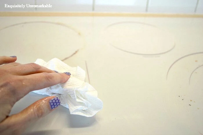 A hand cleaning a glass stove top with a paper towel