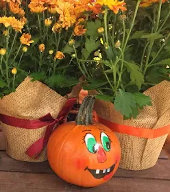 Decorated pumking infront of flower pots.