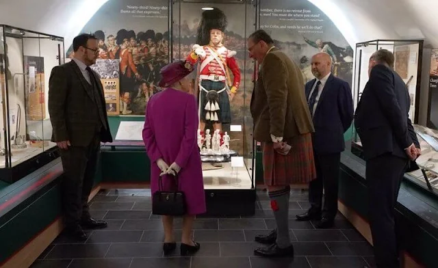 The Queen wore a floral print dress and purple coat and purple hat. diamond brooch