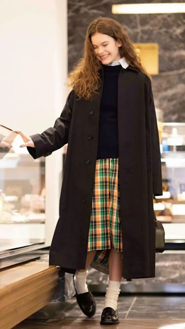 A woamn wear a black coat, a plaid skirt and a colorful scarf.