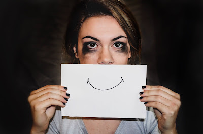 Weary woman holding drawn smile up in front of her mouth