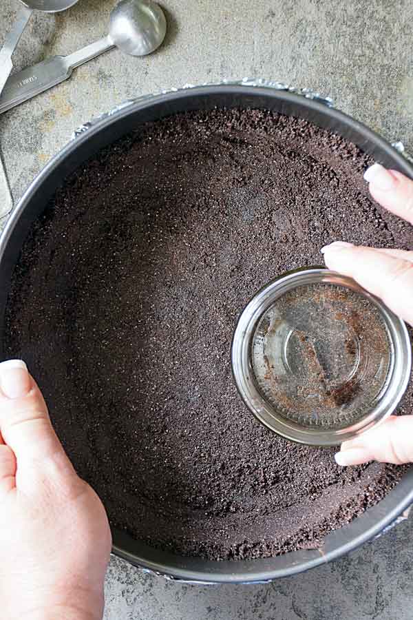 Pressing oreo crumb cookie crust into springform pan for White Chocolate Raspberry Cheesecake