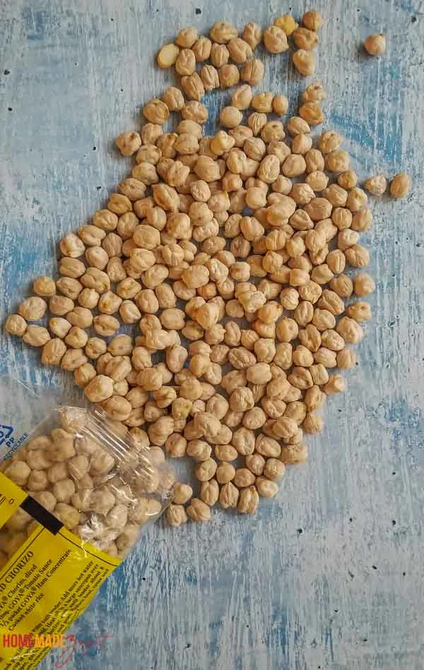 Dried, uncooked chickpeas poured out of the pack on a blue background