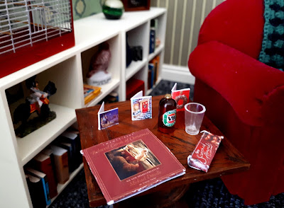 One twelfth scale modern miniature side table containing three traditional Christmas cards, a bottle of beer and a glass, a box of Scorched Almonds and a record of Christmas carols.