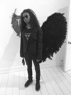 blck and white photo of a young woman dressed in black and wearing dark glasses and black feathered wings