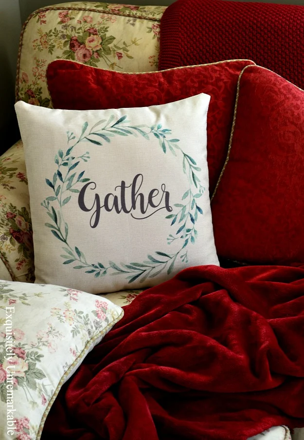 Floral couch with red pillows and tan pillow with green wreath that says Gather