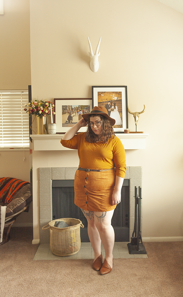 An outfit consisting of a brown panama hat, yellow brown top tucked into a brown button down mini skirt, and brown d'orsay flats.