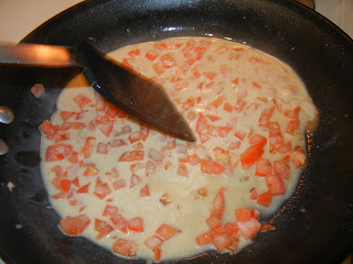 cream and tomatoes in a pan with a spatula stirring it around 
