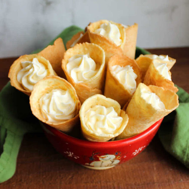 Scandinavian krumkake cookies are crunchy and delicious treats that are cooked on the stove instead of the oven. Fill them with whipped cream, fruit or frosting for an extra special dessert. bowl of Russian buttercream filled krumkake horns