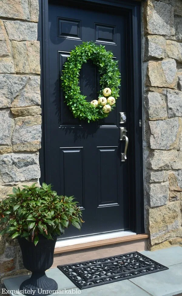 Black door, black planter, black mat with green boxwood pumpkin wreath on door