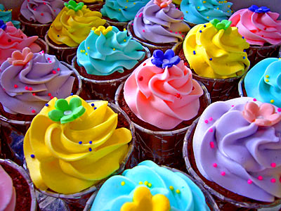 close up of many cupcakes with bright frosting and candy flowers on top