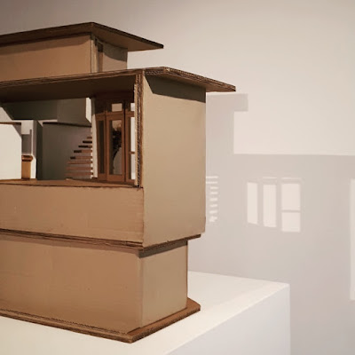 Part of a cardboard model of The Paterson House designed by Enrico Taglietti, on a plinth in an art gallery, casting a shadow onto the wall behind it.