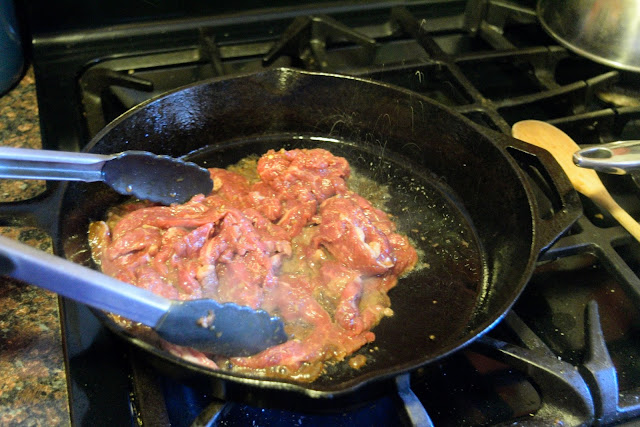 The marinated beef being added to the hot skillet. 