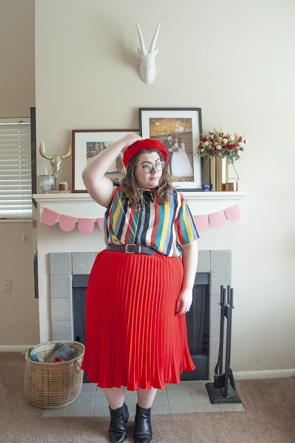 An outfit consisting of a red beret, a multicolor short sleeve collared top top tucked into a red pleated midi skirt and black ankle boots.