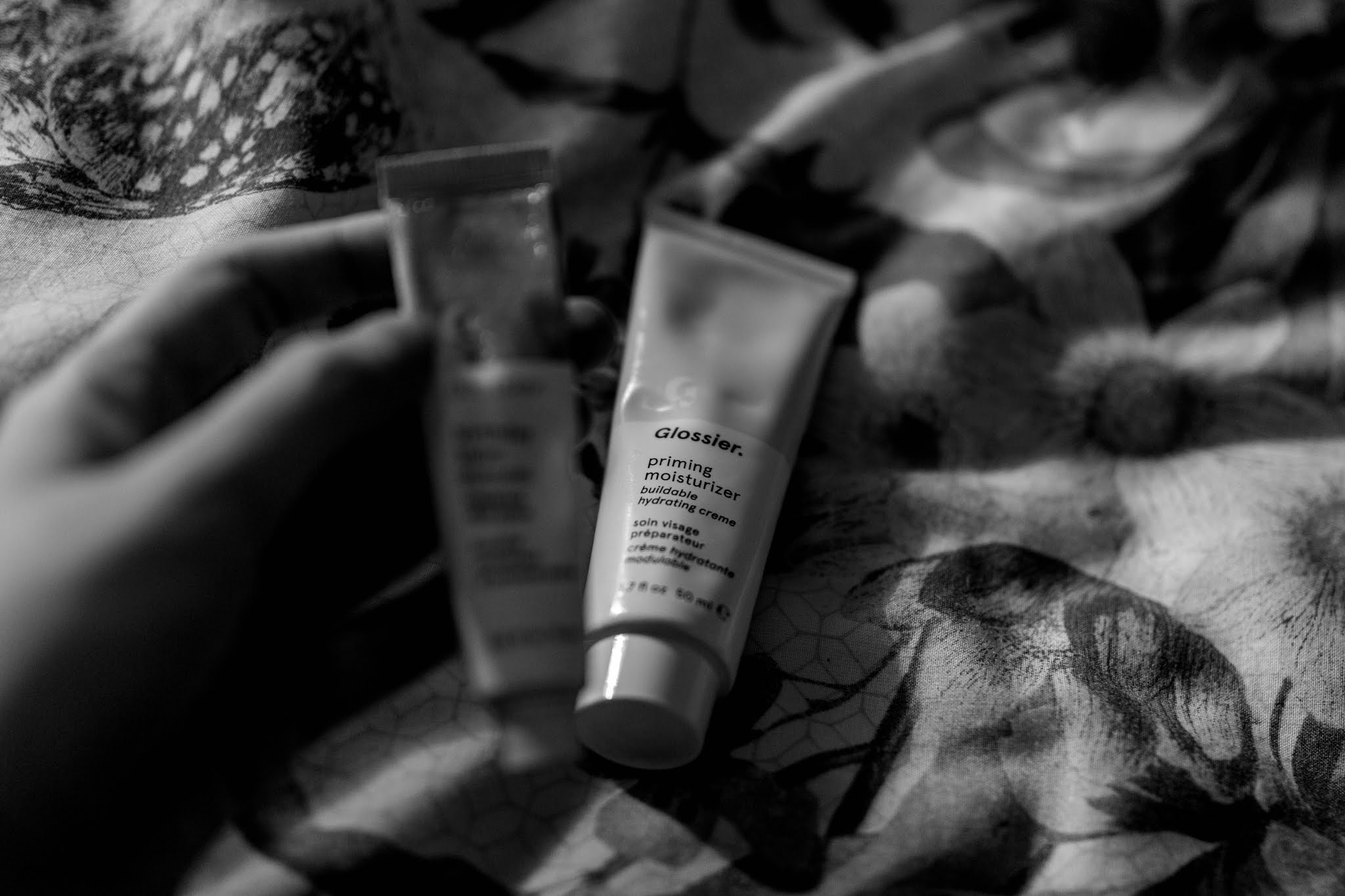 black and white photos of glossier beauty products on floral bedding