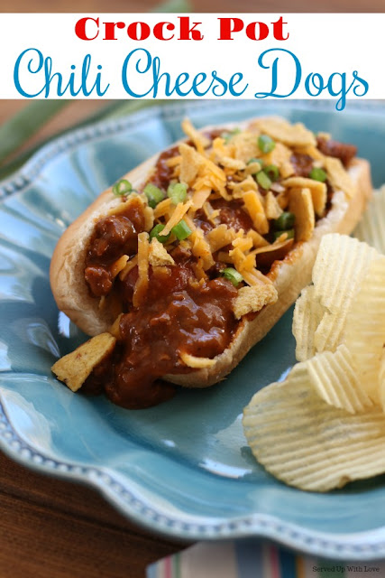 Hot dog covered in chili with cheese on bun served up on a blue plate alongside some chips