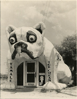 A black-and-white photograph of a restaurant shaped like a bulldog. "TAMALE" is written on the bulldog's left leg. "ICE CREAM" is written on the bulldog's right leg.