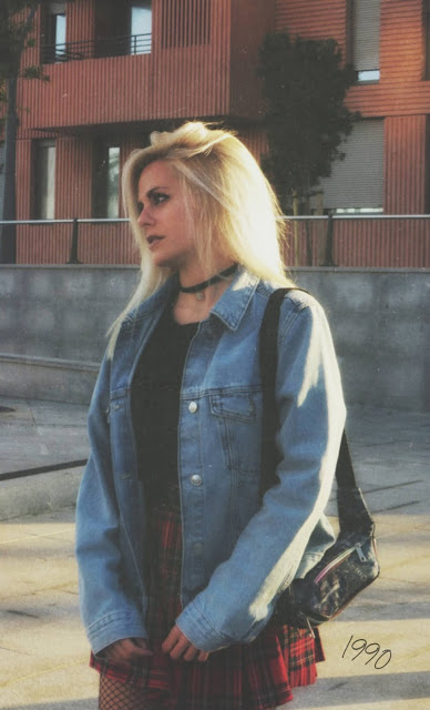 Estilo grunge con camiseta negra, falda de tablas tartán, medias de red grande, botas estilo militar y cazadora vaquera