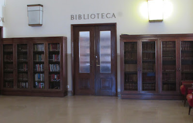 estantes de madeira com livros, porta dupla de madeira e vidro e a palavra biblioteca na parede