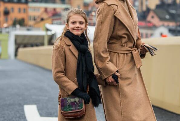 Crown Princess Victoria wore a camel coat by Max Mara, and gold earrings by Sophie by Sophie. Princess Estelle. By Malene Birger clutch