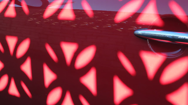 Red car door with silver handle and patterns of light made by fancy wall near by