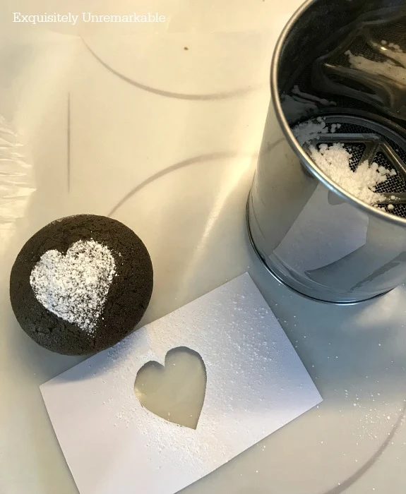 Valentine's Day Cupcake with powdered sugar heart, flour sifter and heart stencil on the stove