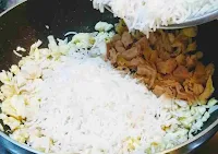 Adding boiled rice over scrambled eggs and Chicken pieces for making chicken fried rice recipe