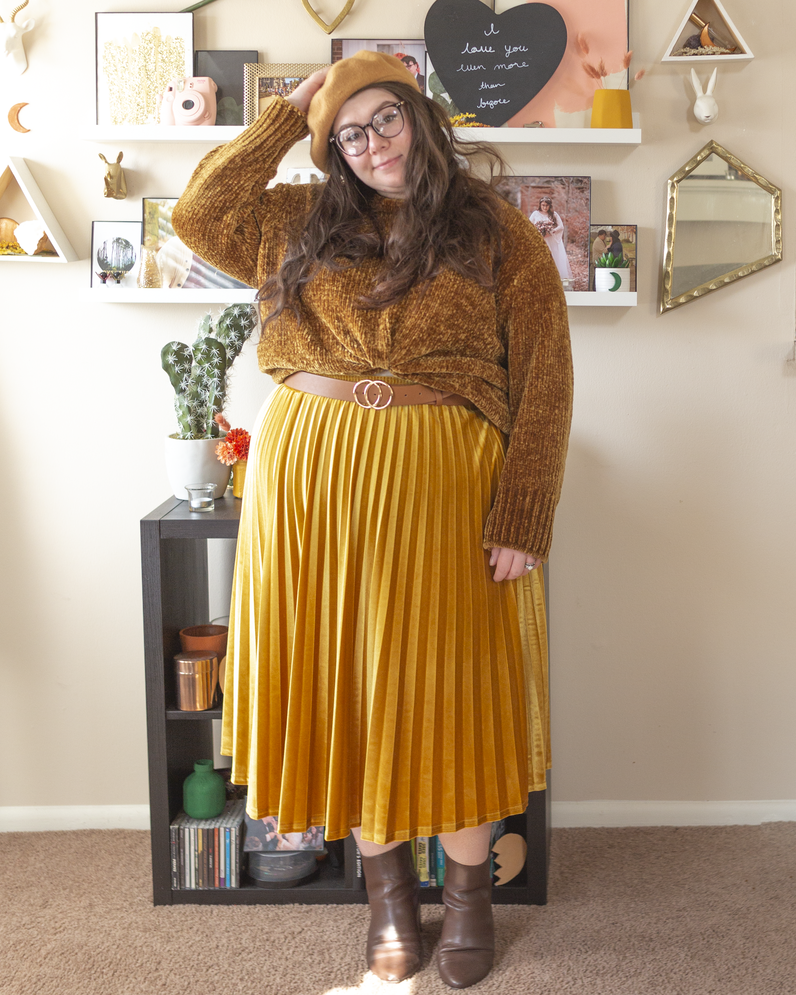 An outfit consisting of a tan beret, a dark yellow chenille sweater tucked into a mustard yellow velvet pleated midi skirt and brown midi boots.