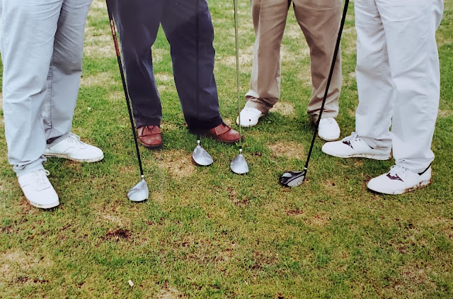 image of four peoples feet and their golf clubs