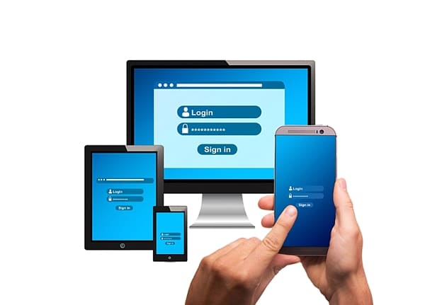 Mãos segurando smartphone com tela de login computador e tablet de fundo