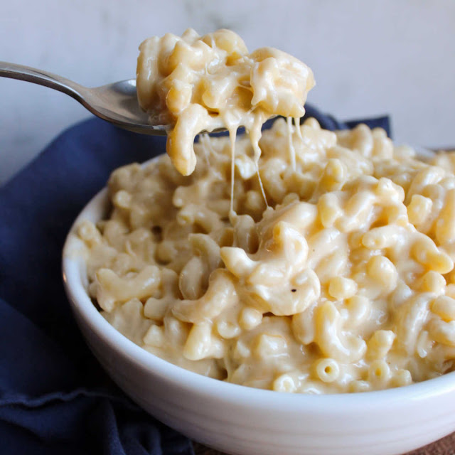 This is the creamiest stovetop macaroni and cheese recipe ever! It is good on it's own or stir in some ham for a simple family pleasing dinner. spoon lifting big scoop of creamy mac and cheese out of serving bowl