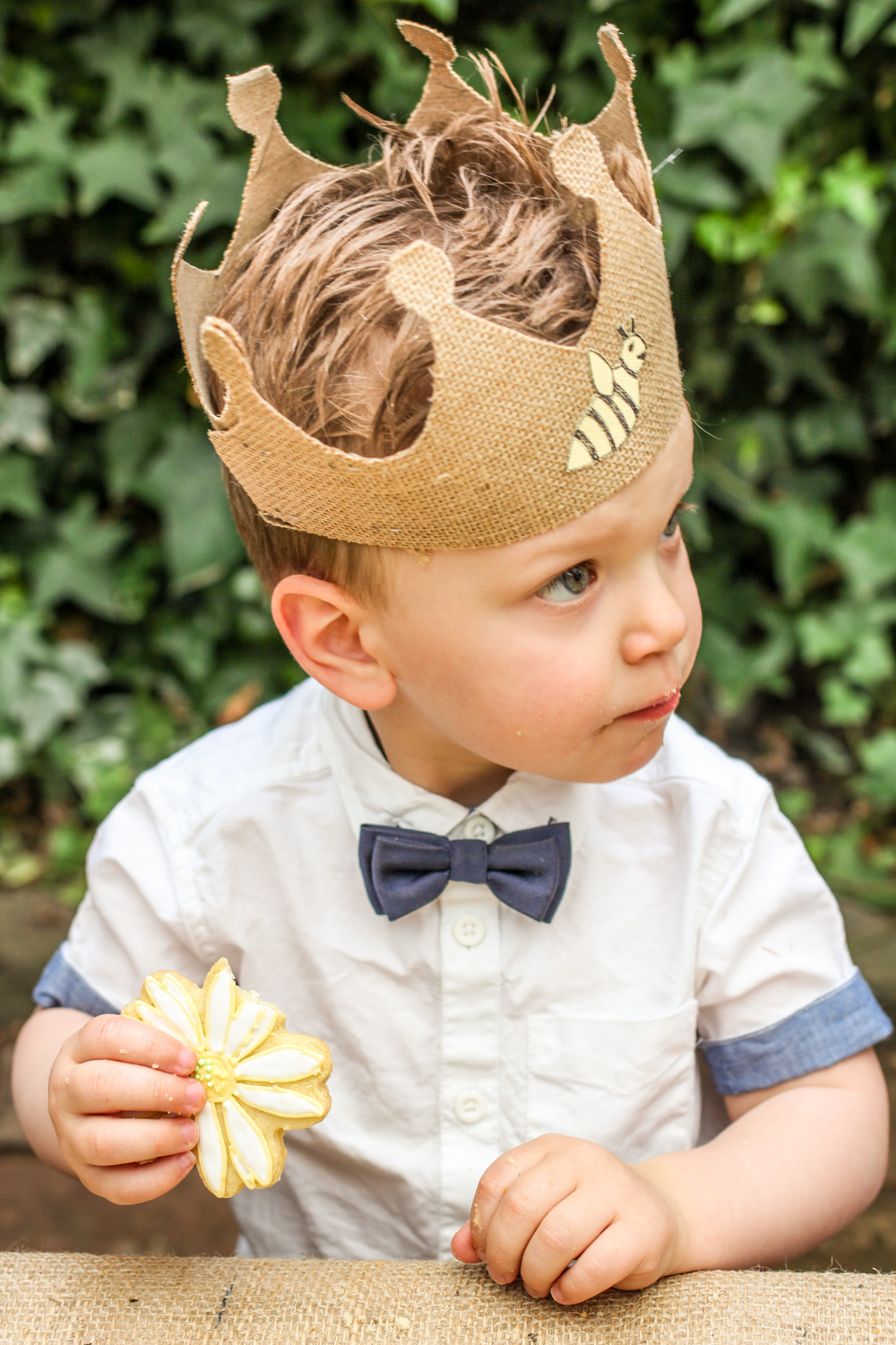 Birthday boy wearing bumble bee crown and bow tie whilst eating a daisy flower cookie For more boys and unisex kids first birthday party inspiration visit the Goldfields Girl blog