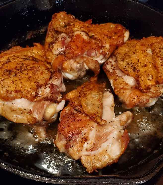 chicken thighs frying in cast iron skillet