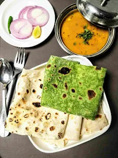 Serving plain and palak rumali folded with curry, onion slice, fork and spoon in background