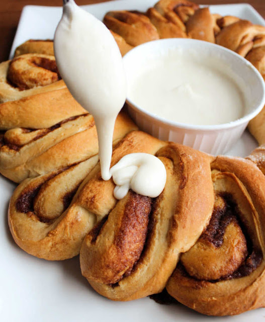 Soft and sweet cinnamon rolls take on a festive wreath shape. They are a perfect holiday breakfast or something fabulous for overnight guests. spoon drizzling icing over warm cinnamon rolls