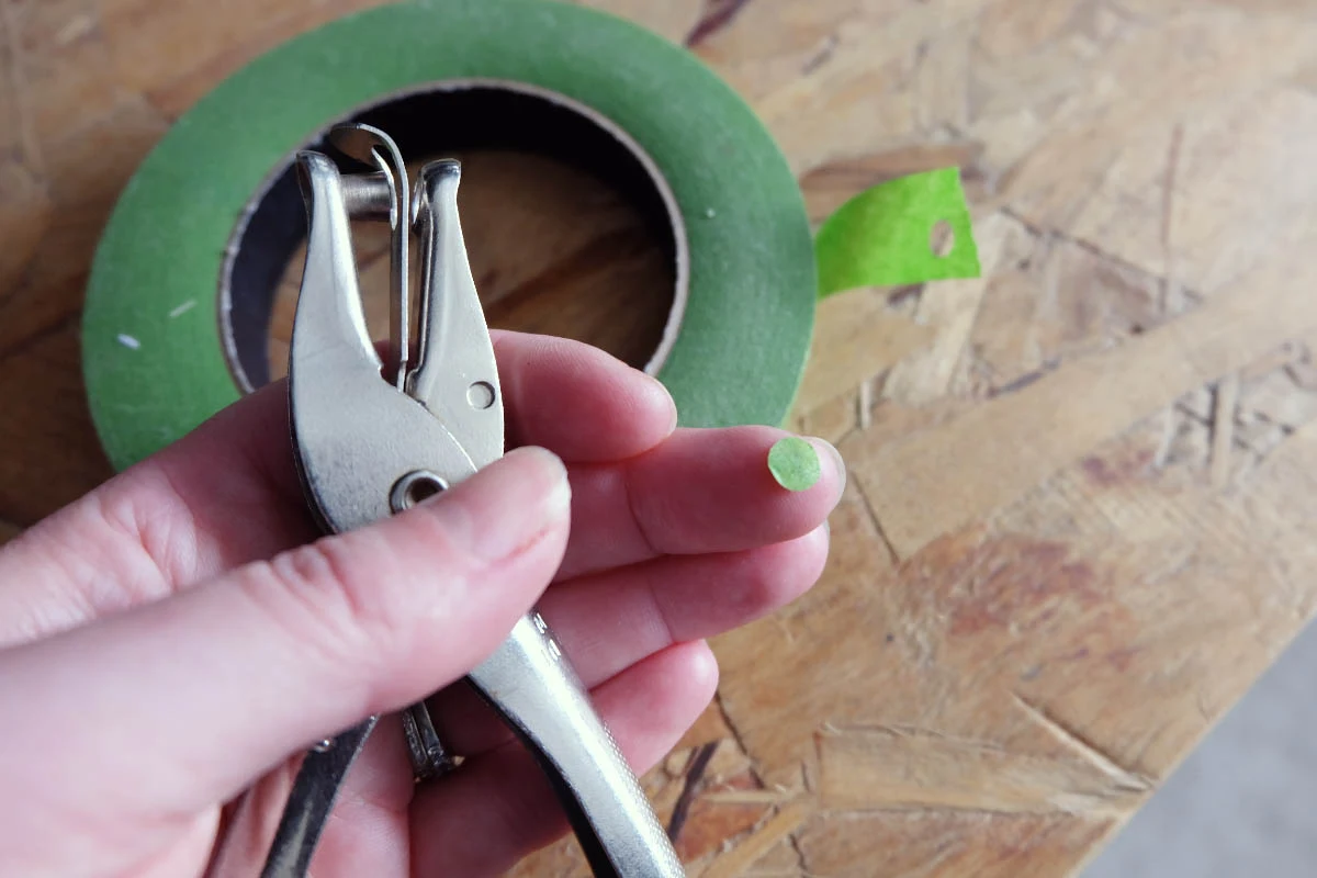 single hole punching painters tape to mark wall for nails