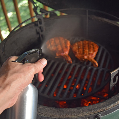 Spritzing apple juice and bourbon onto thick pork chops on the Big Green Egg kamado grill.