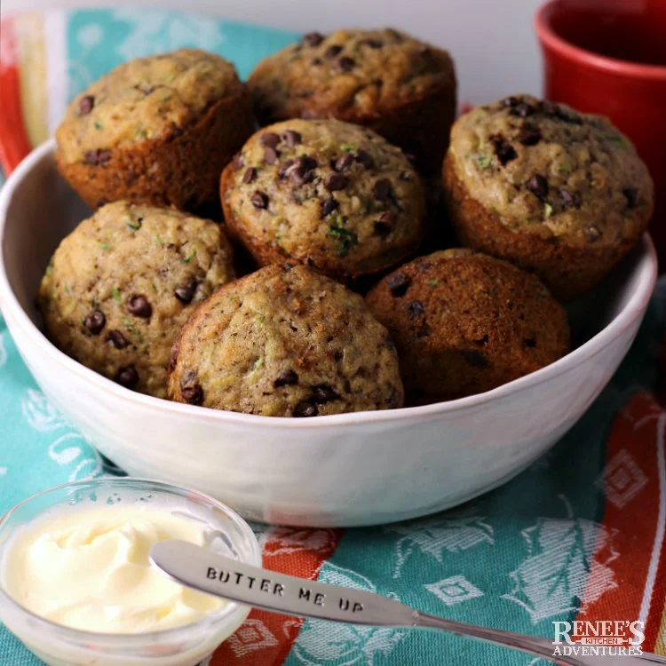 Chocolate Chip Zucchini Muffins by Renee's Kitchen Adventures in a bowl and a knife for spreading butter resting on a small bowl of butter