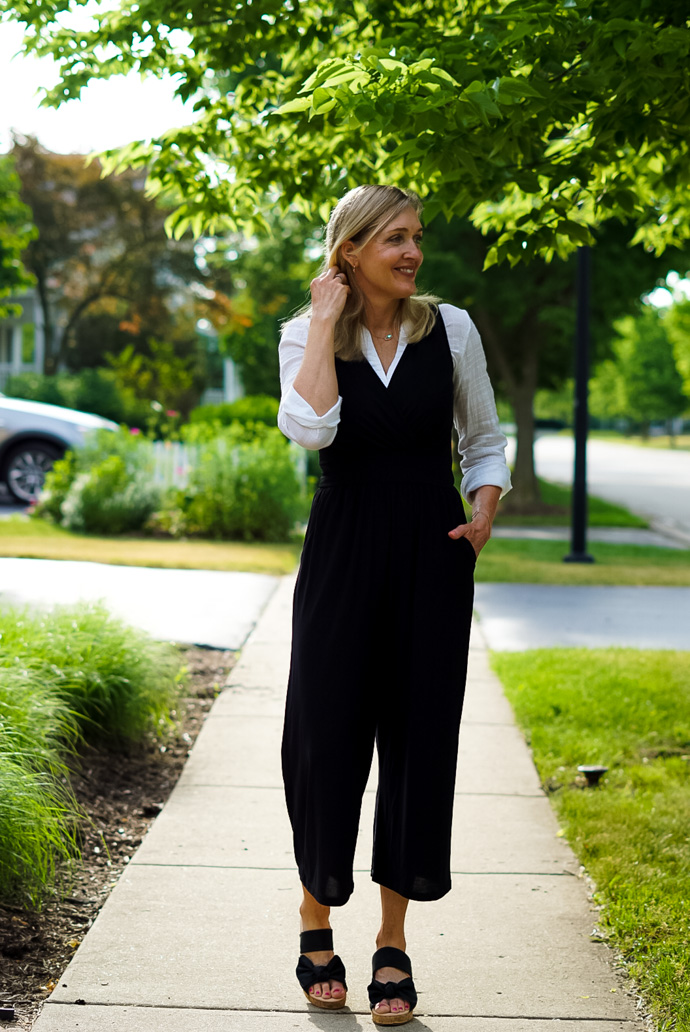 A woman wears a white collared shirt over a sleeves black jumpsuit