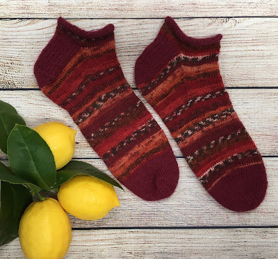 Hand-knitted socks with rolled cuffs and asymmetrical toes laid next to 3 lemons
