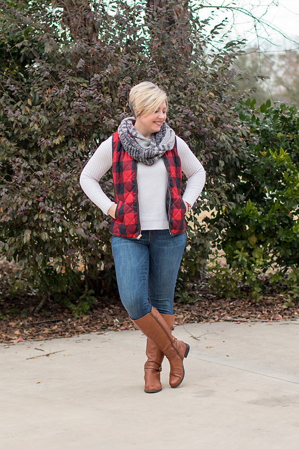 Winter outfit of white sweater, plaid vest, infinity scarf, blue jeans and brown boots