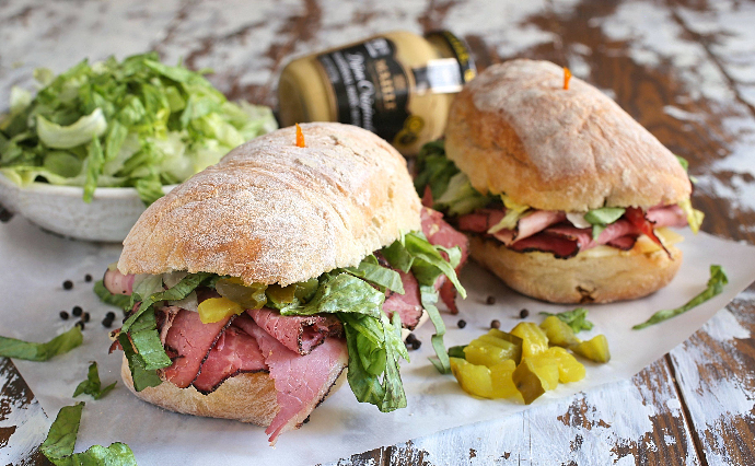 Recipe for an over-stuffed sandwich filled with pastrami, Swiss cheese, shredded lettuce, diced pickles, mayo and mustard on toasted Ciabatta rolls.