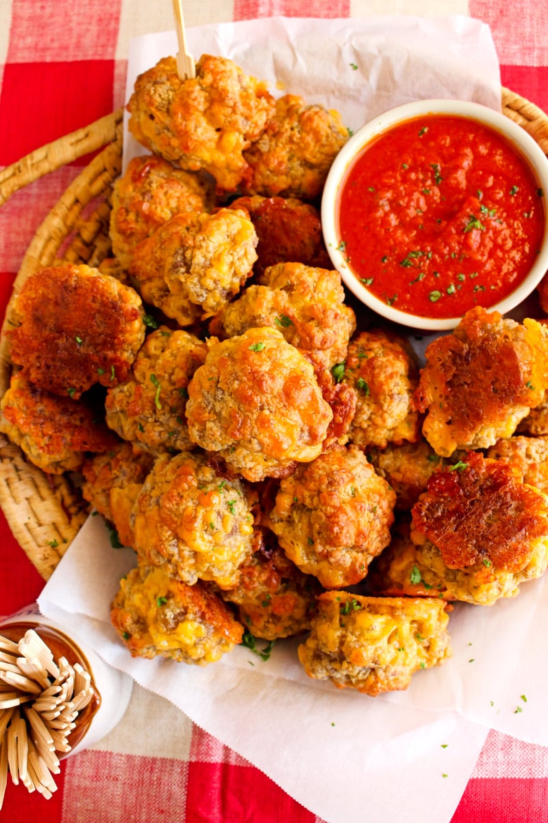Top view of sausage balls and marinara sauce on plate on a red checkered tablecloth.