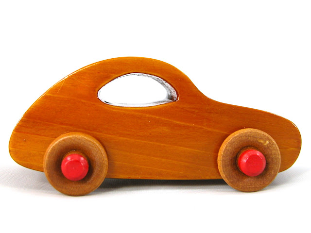 A small handmade wooden toy car classic 1957 bug from the Play Pal series made from pine wood and hand finished with amber shellac. The hubs are painted bright red. Small enought to use as a stocking stuffer or cake topper.