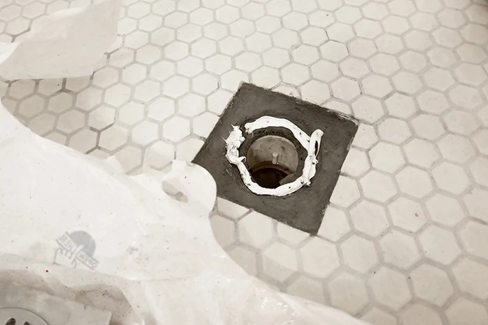 squirting Gorilla construction adhesive on cement in drain