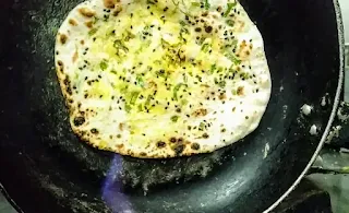 Cooking paneer kulcha over direct heat flame by flipping the tawa with paneer kulcha