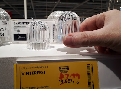 Selection of IKEA Vinterfest LED decorative lighting piecs on display above a sign withthe price marked down from $9.99 to $7.99. A hand is picking up one of the lights to show the size of them.