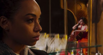 Logan Browning looks on as Allison Williams plays the cello in a stunning red dress in Netflix's 2019 original film The Perfection