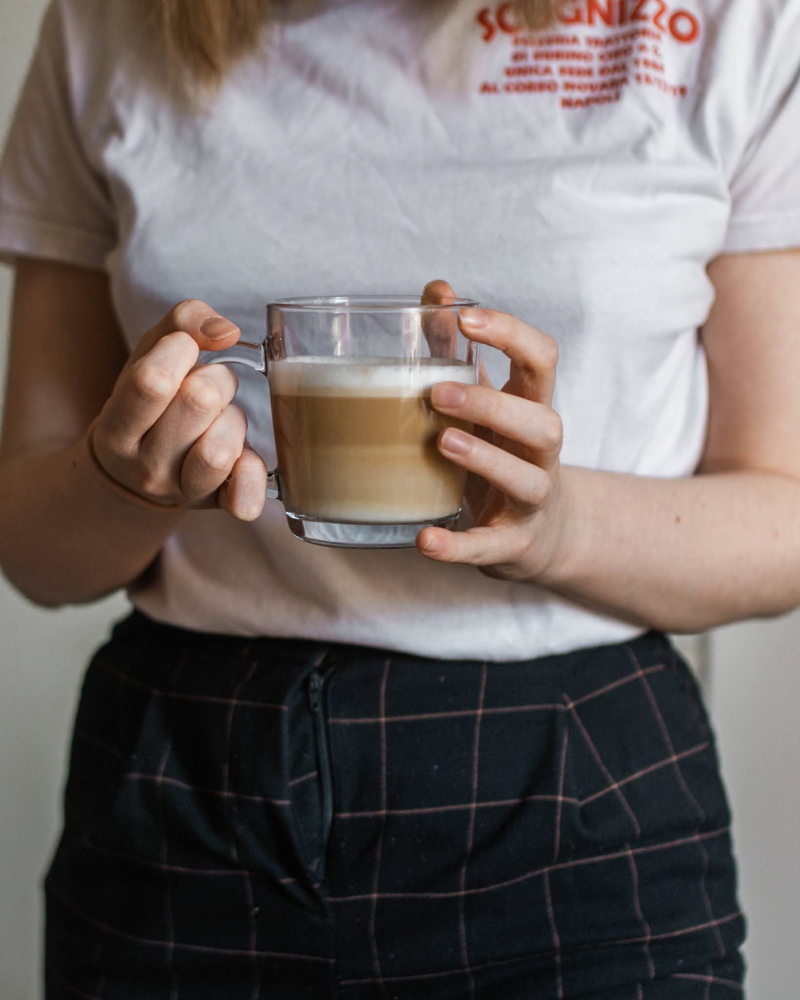 girl holding latte in glass mug wearing a white tshirt